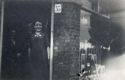 818217 Afbeelding van Mientje Wouda in de deuropening van de kruidenierswinkel van haar ouders (Pelikaanstraat 35) te ...